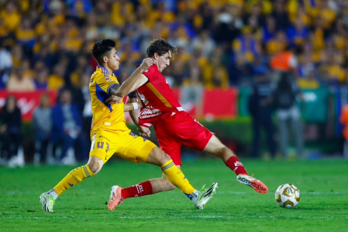 Jugador del Toluca disputa el balón ante un rival de Tigres durante un intenso duelo de la Liga MX, marcado por la presión y el choque físico en medio campo.
